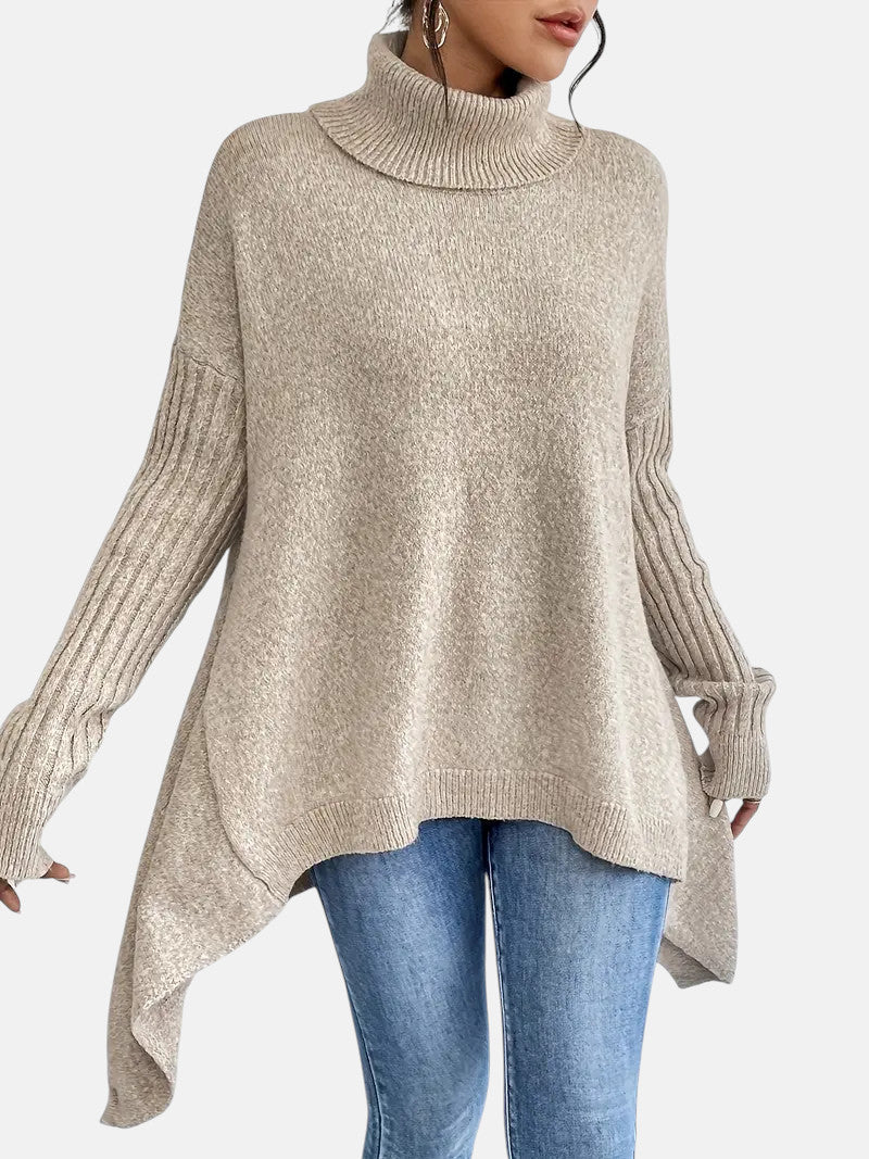 Beige long turtleneck sweater with ribbed sleeves and asymmetrical hem paired with blue jeans.