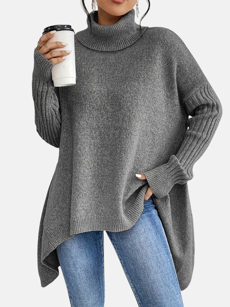 Grey long turtleneck sweater with ribbed sleeves, asymmetrical hem, worn over blue jeans.