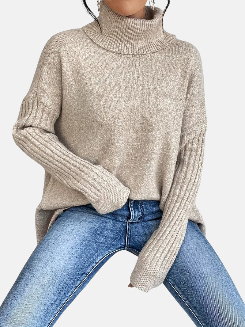 Camel-colored long turtleneck sweater with ribbed sleeves and relaxed fit paired with blue jeans.