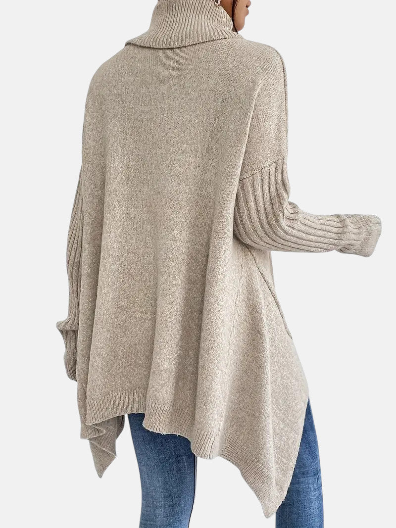 Beige long turtleneck sweater with ribbed sleeves and asymmetric hem worn with blue jeans.