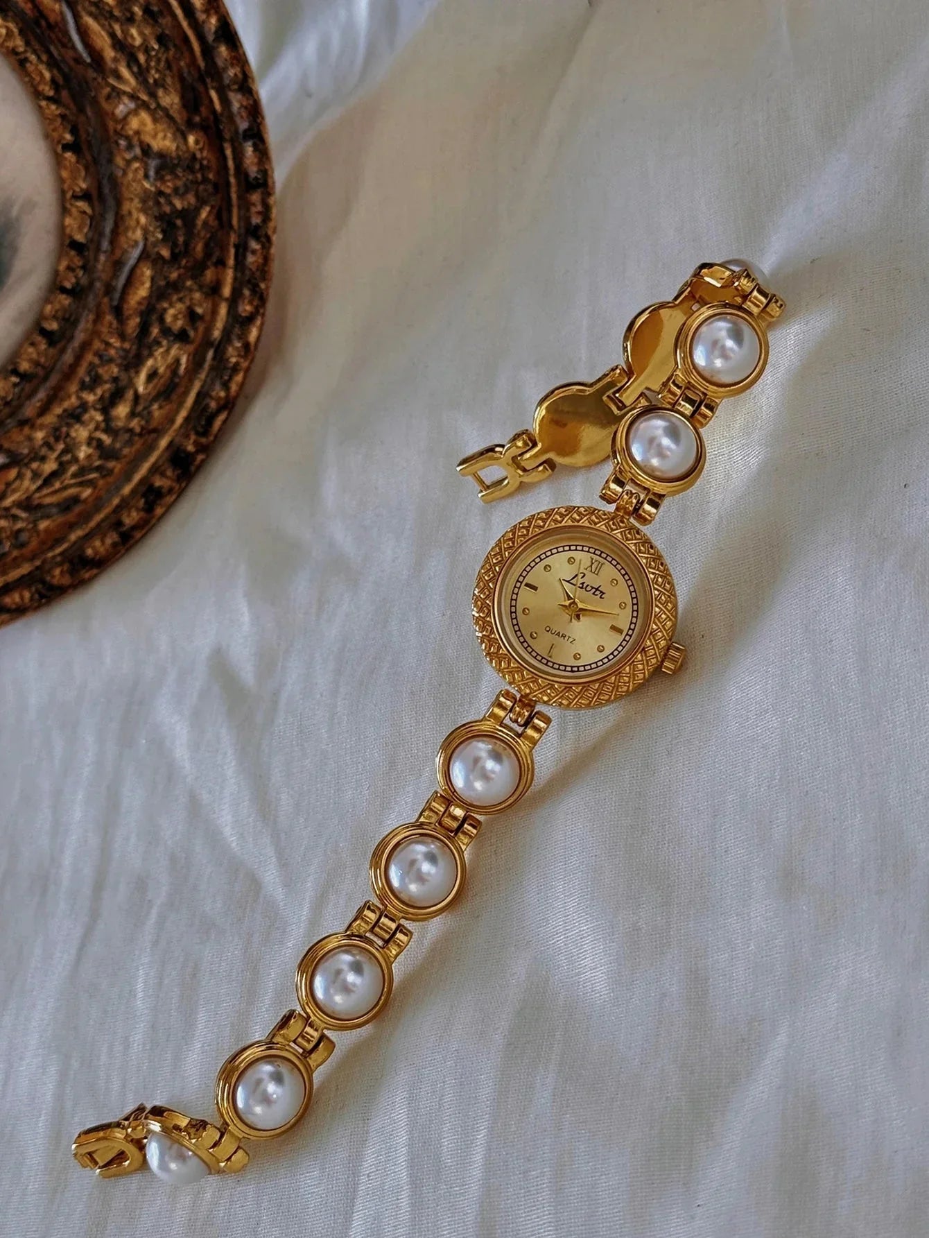 Gold bracelet with pearl accents on a white fabric background