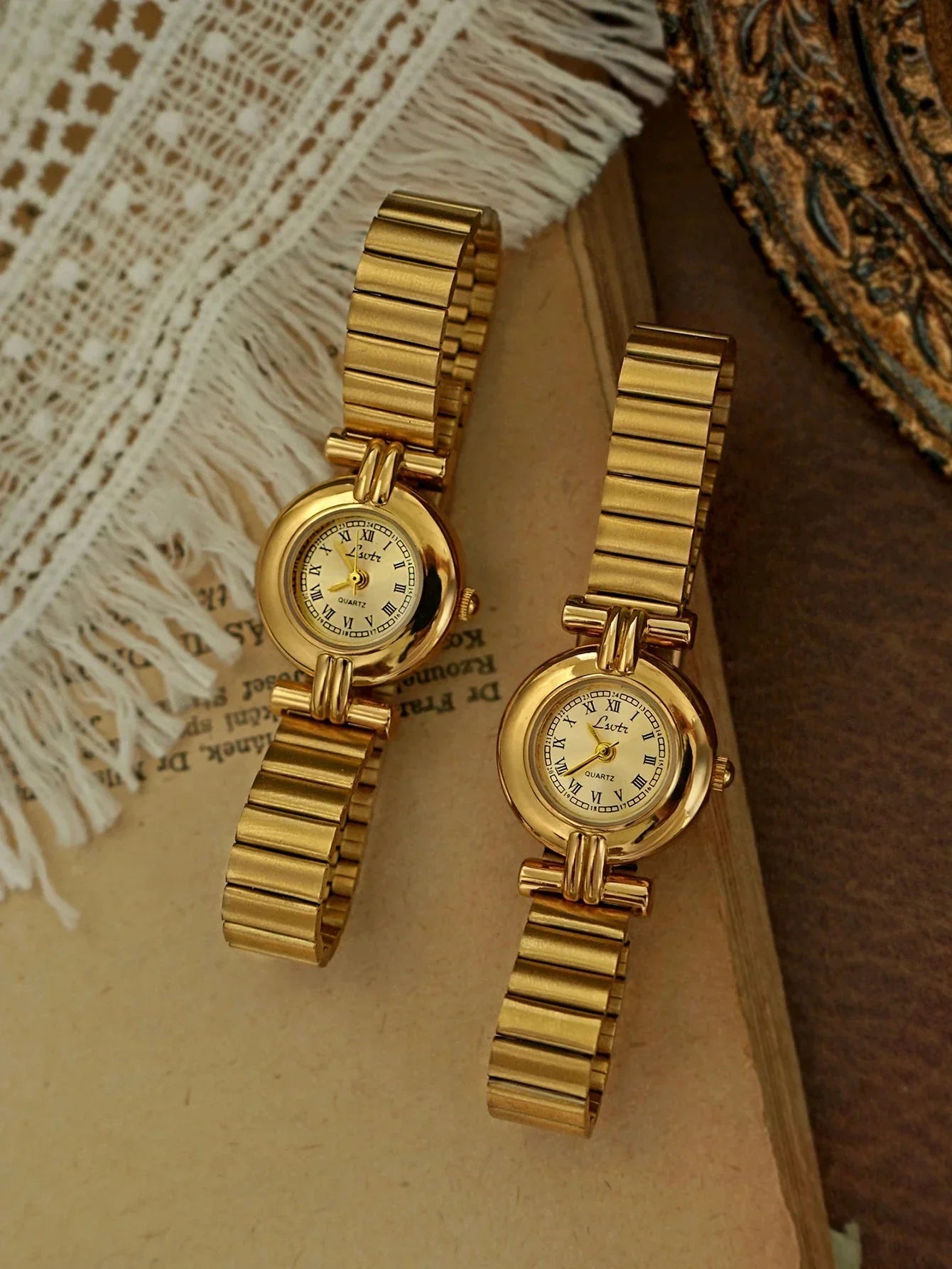 Two gold wristwatches on a textured surface with a decorative background