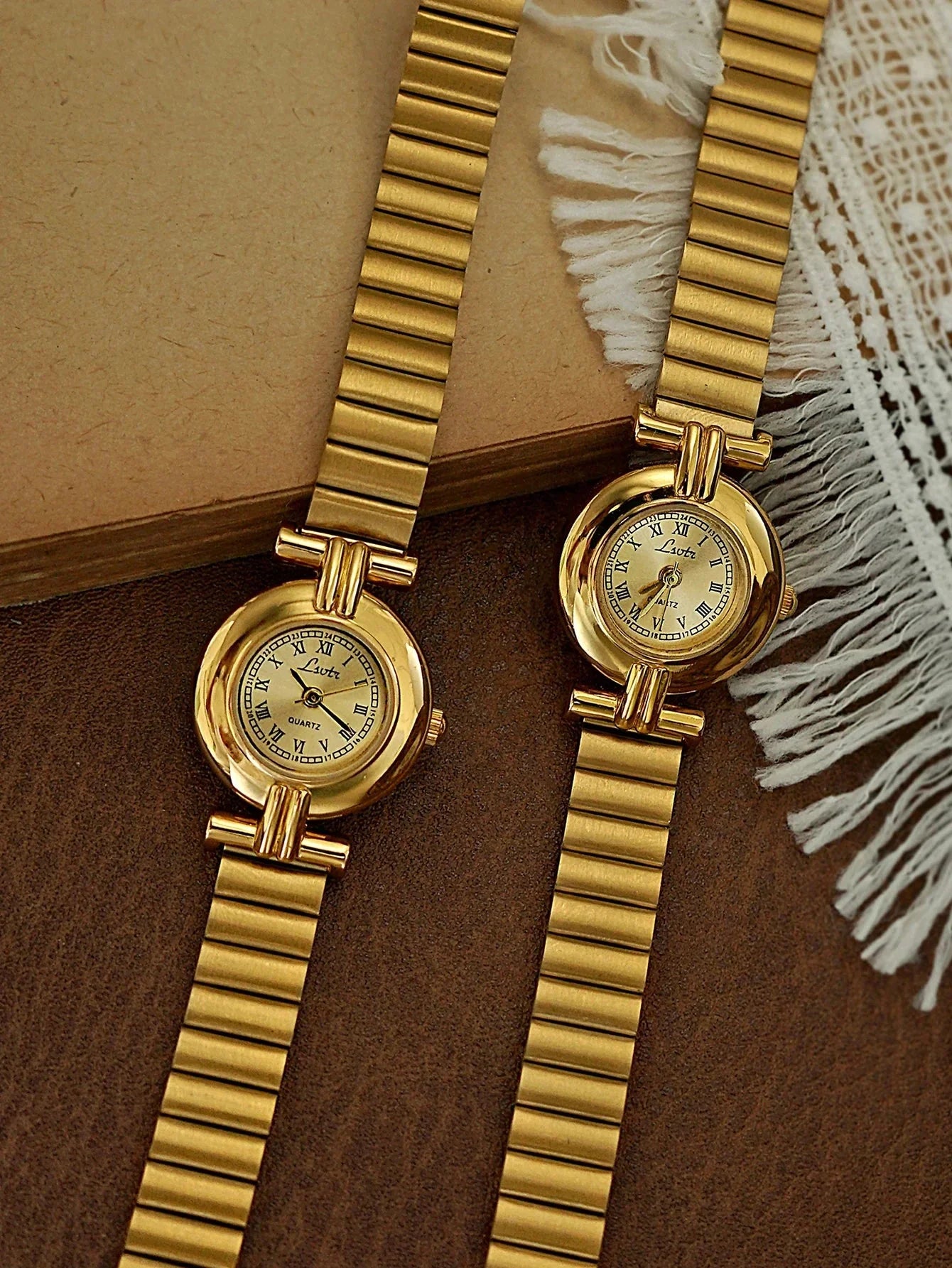 Two gold watches on a textured surface with a neutral background