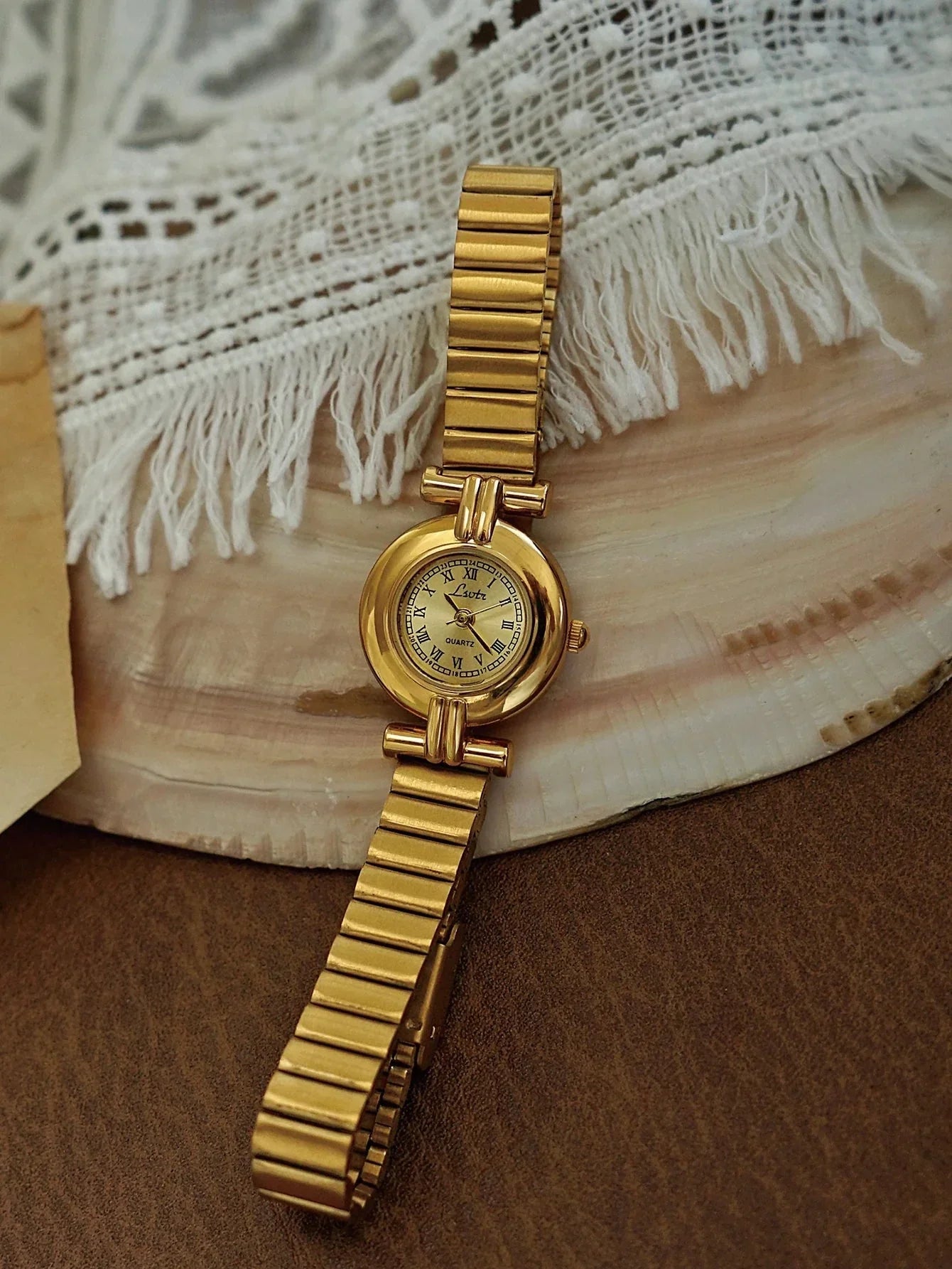 Gold wristwatch on a textured surface with lace fabric in the background