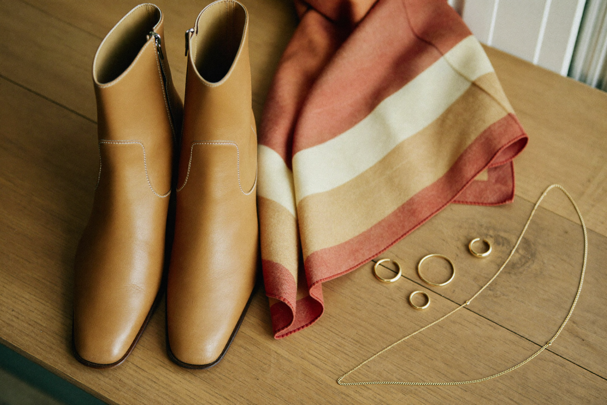 Transitional outfit flat lay with camel ankle boots, terracotta scarf and gold jewellery