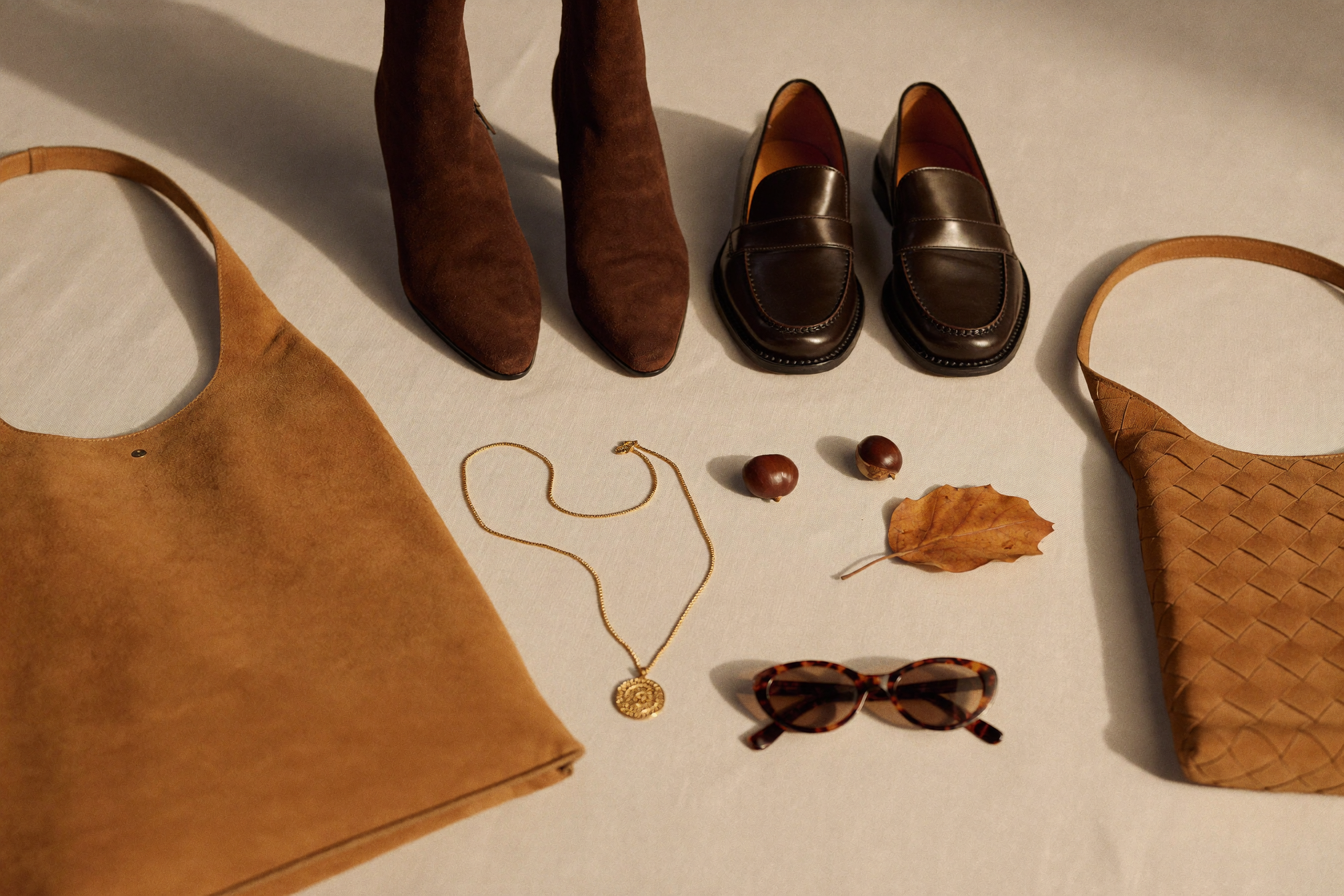 Autumn 2026 fashion trends accessories flat lay with brown suede ankle boots, leather penny loafers, suede tote bag and gold chain necklace