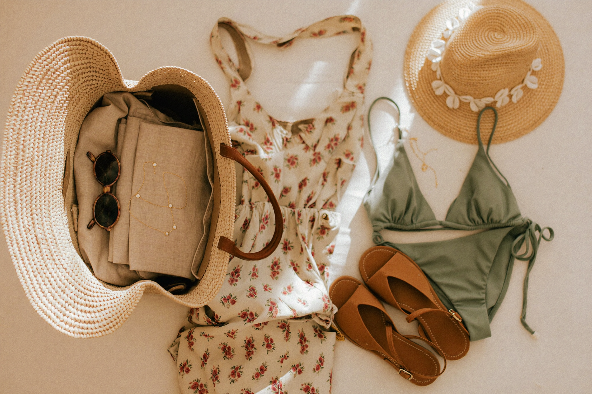 Holiday capsule wardrobe flat lay: straw weekender bag packed with linen co-ord, swimwear, sandals and straw hat