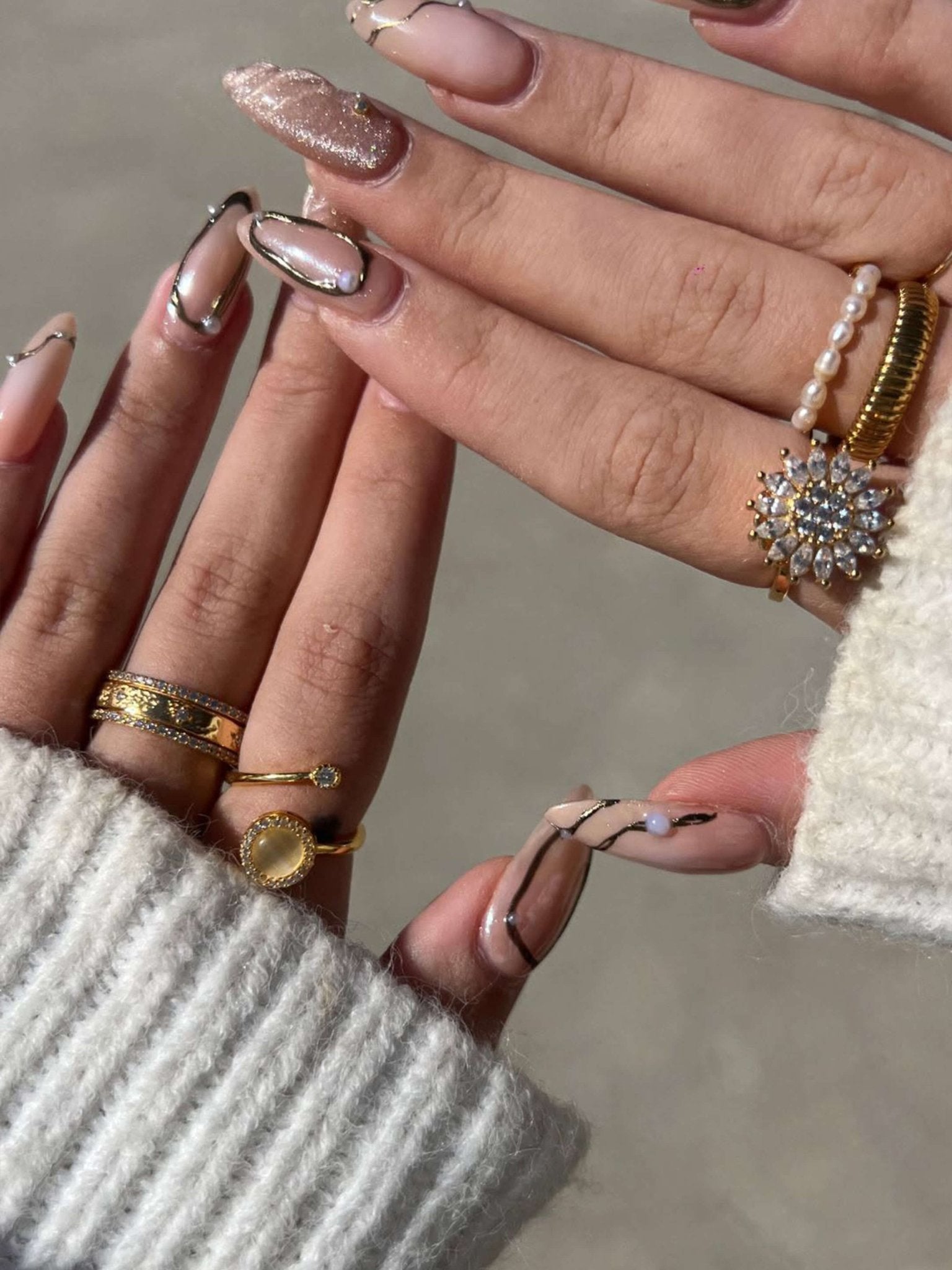 Close-up of hands with nail art and jewelry against a neutral background