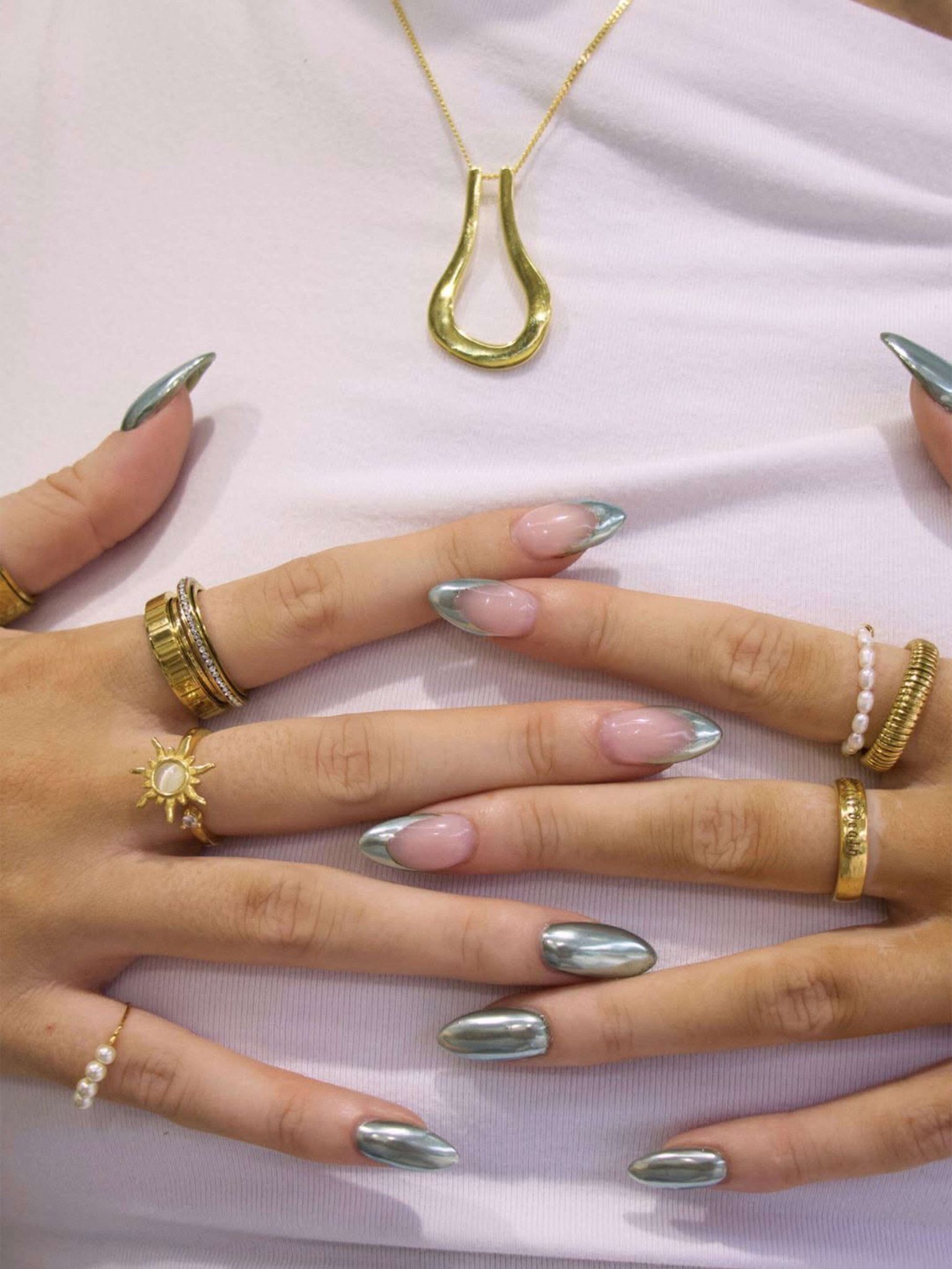 Close-up of hands with silver nail polish and gold jewelry on a white background