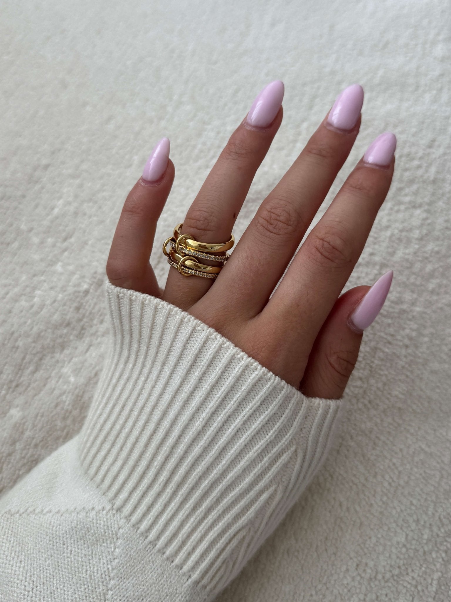 Hand with pink nail polish wearing a gold ring on a light background