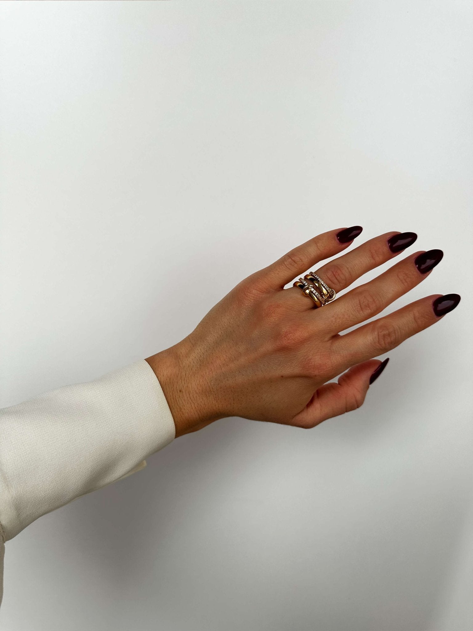 Hand with dark nail polish wearing a ring on a plain background