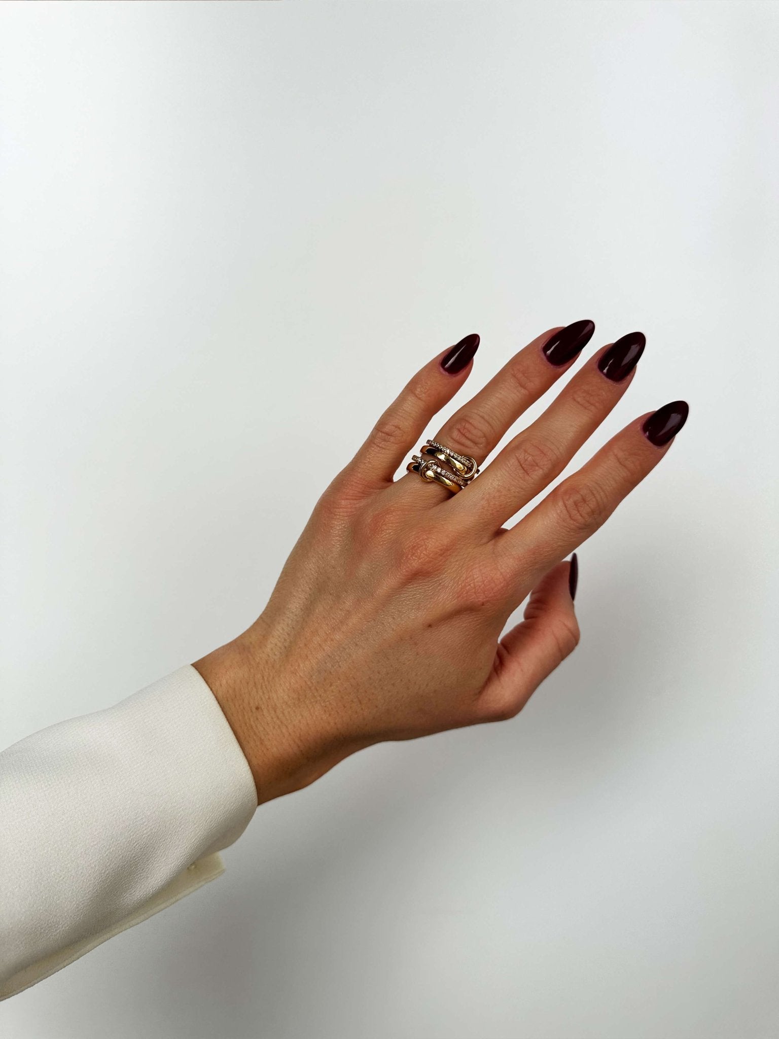 Hand with dark nail polish wearing a gold ring on a white background