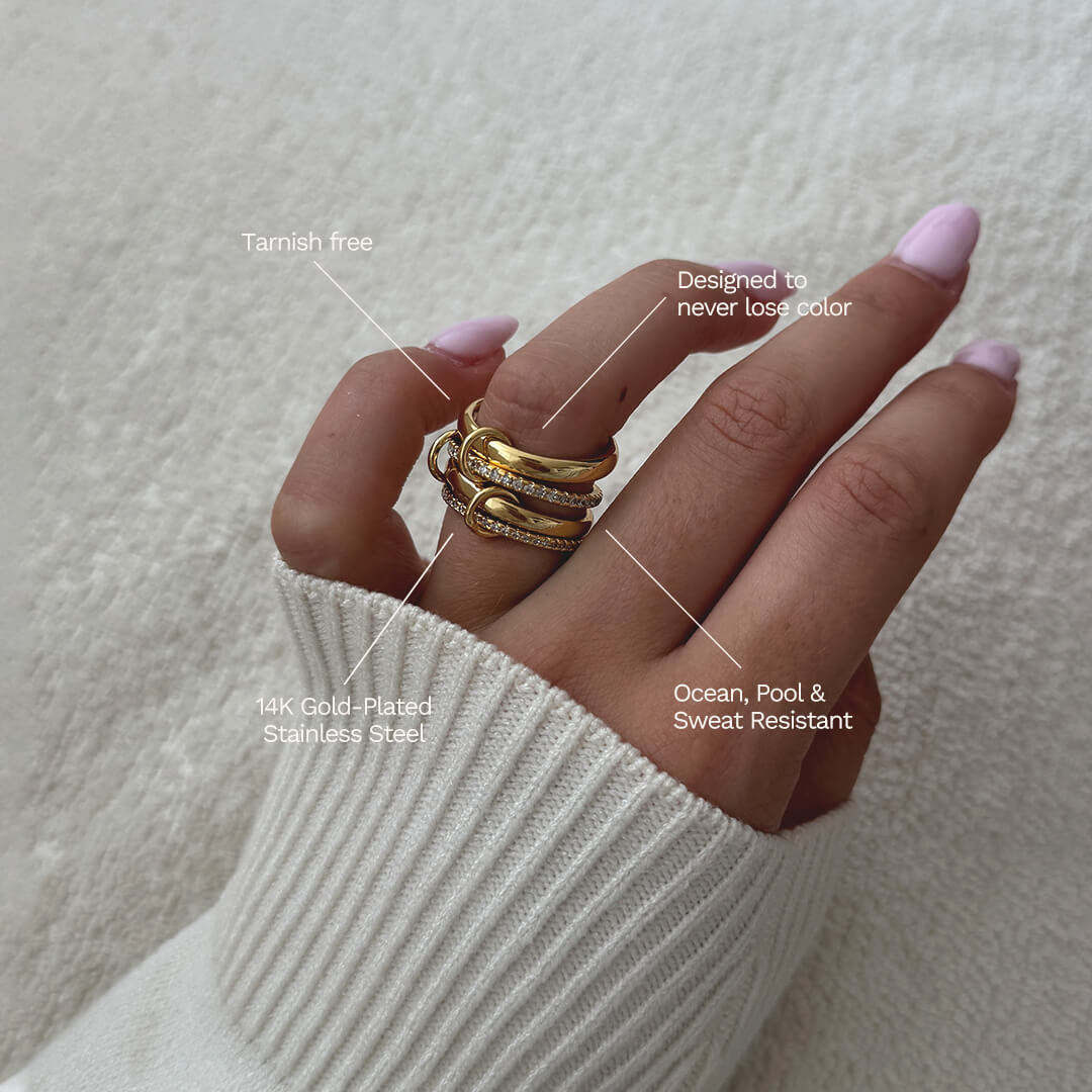 Hand wearing gold rings with text highlighting features on a neutral background