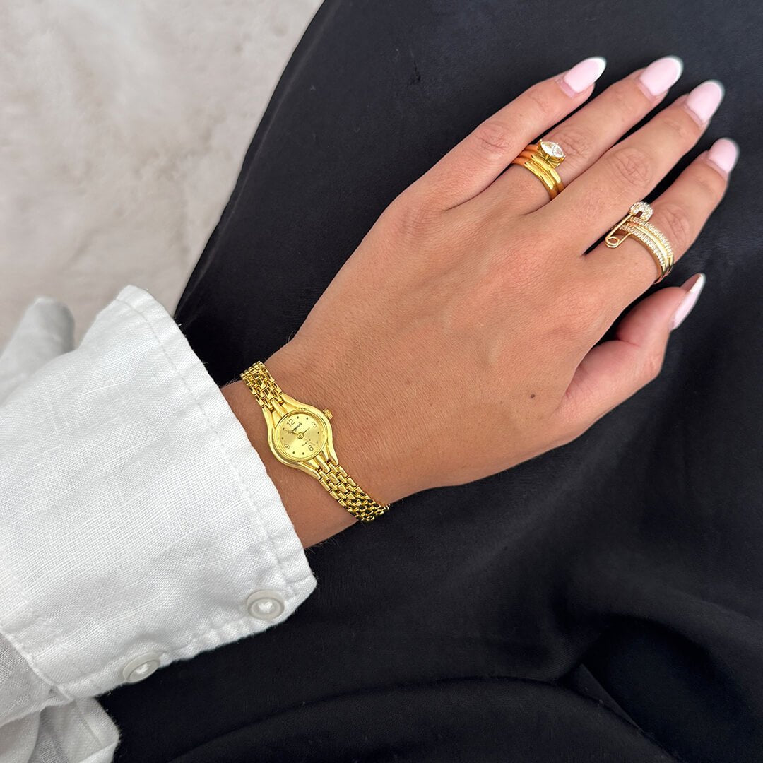 Hand wearing a gold bracelet and rings on a black background