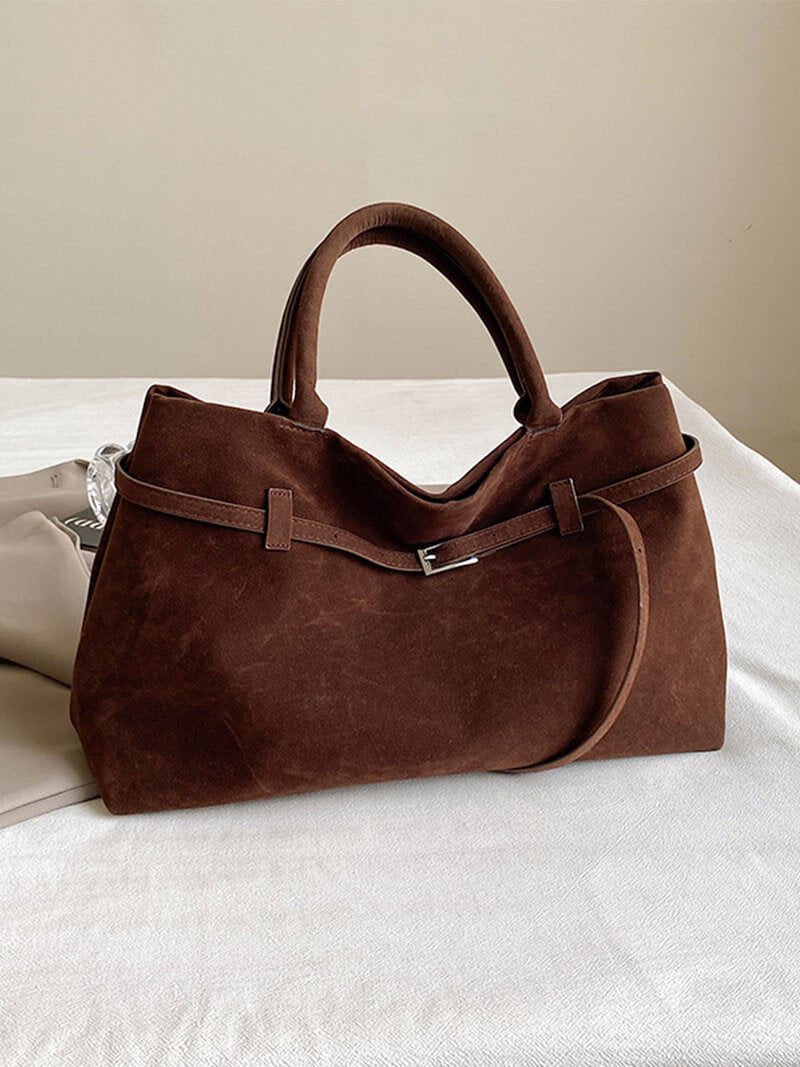 Brown leather handbag on a white surface with a neutral background